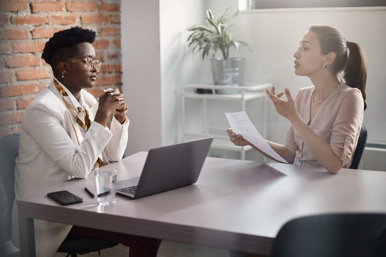 Young woman communicating with African American human resource manager while applying for job at corporate office.